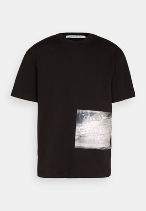 Czarna koszulka Calvin Klein Jeans z krótkim rękawem, z błyszczącą, prostokątną srebrną naszywką z logo na dolnej przedniej prawej stronie.