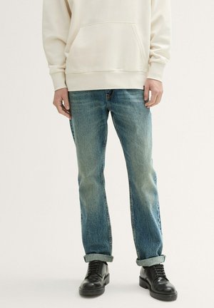 Jeans de mezclilla azul claro con un corte recto, ligeramente desgastados, con dobladillo en el tobillo. Combinados con una sudadera color crema y botas negras con cordones.