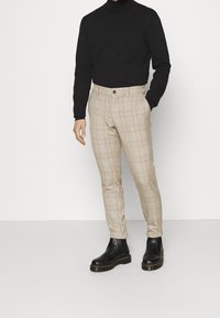 Béžové kárované kalhoty s úzkým střihem a hnědým zapínáním na knoflík. Kombinované s černým rolákem a černými kotníkovými botami.