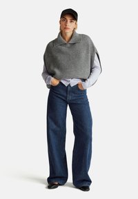 Šedý uplétaný pončo s širokým límcem přes světle fialovou košili s dlouhým rukávem, kombinované s vysokými, volnými džíny z tmavého denimu.