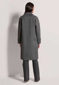 Grau wollener Mantel mit geradem Schnitt, großem Kragen und aufgekrempelten Ärmeln. Getragen über dunklen Schlagjeans, die ein elegantes, minimalistisches Design zeigen.