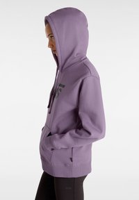 Felpa con cappuccio viola realizzata in tessuto liscio, presenta una tasca frontale e un grande logo stampato in nero. Cappuccio con cordoncino regolabile.
