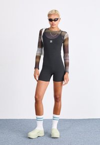 Černý bezrukávový body s žebrovanou strukturou, bílé logo Adidas, nošený pod průhledným dlouhým rukávem s více barvami, doplněný mátově zelenými pantofli.