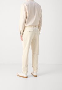 Kremowe flanelowe spodnie o teksturowanym wykończeniu, z tylnymi kieszeniami i detalem w postaci guzika, zestawione z jasnobeżową bluzką z długim rękawem.