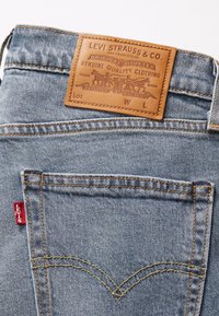 Lyseblå denimjeans med et lærpatch merket "Levi Strauss & Co." og oransje sømmer. Har to baklommer. Rød Levi's-lapp synlig.