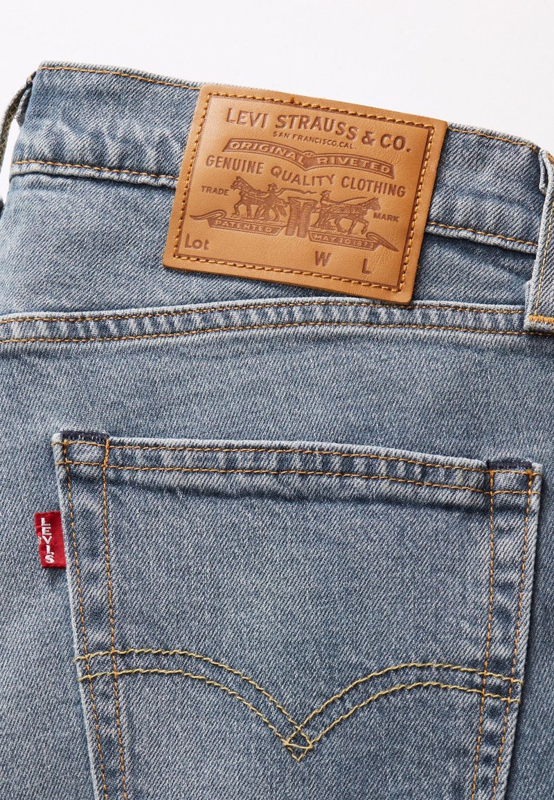 Jeans de mezclilla azul claro con un parche de cuero que dice "Levi Strauss & Co." y costuras naranjas. Presenta dos bolsillos traseros. Etiqueta roja de Levi's visible.