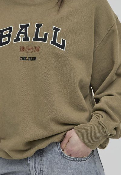 Felpa verde oliva con lettering "BALL" in bianco e nero, caratterizzata da polsini a coste e una vestibilità rilassata, abbinata a jeans grigi chiari.