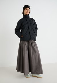 Schwarz gesteppte Jacke mit hohem Kragen, lockerer grauer Rock mit geraffter Taille und helltürkise Sneakers mit weißen Streifen. Minimalistisches Design.
