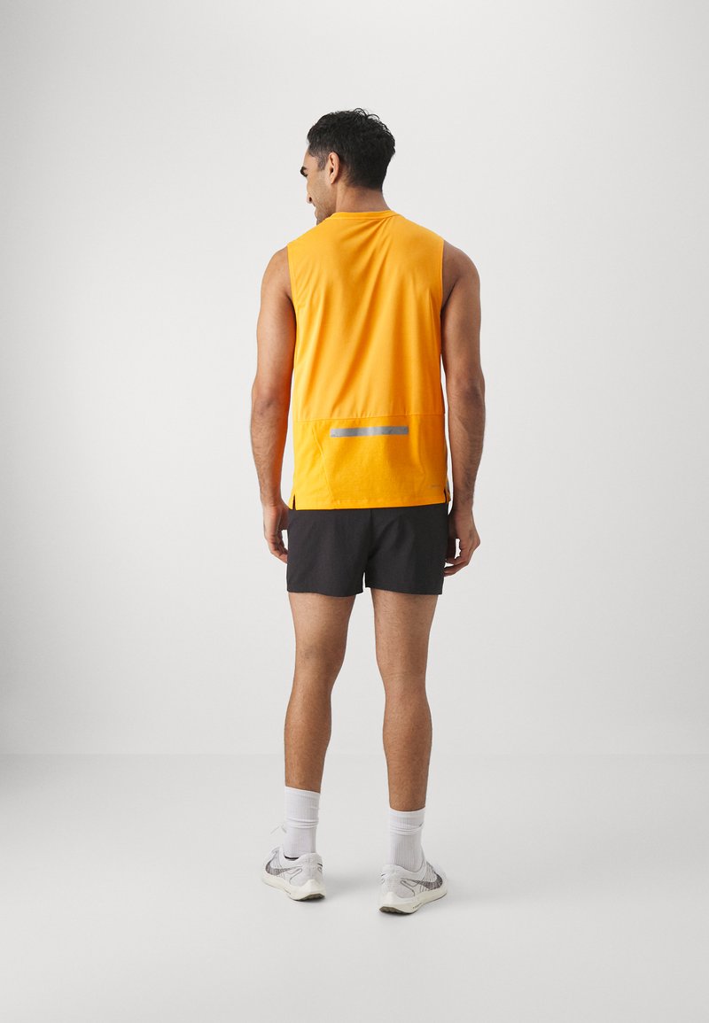 T-shirt sans manches de sport en orange vif avec bande réfléchissante, associé à un short noir. Tissu doux avec une coupe décontractée et des fentes latérales.