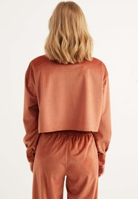 Häkelstil, rostfarbener, cropped Top mit gerippter Textur und langen Ärmeln, kombiniert mit passenden, hoch taillierten Hosen.