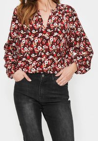 Röd blommig blus med v-ringning och knapplist, med långa puffärmar. Matchas med åtsittande svarta jeans.