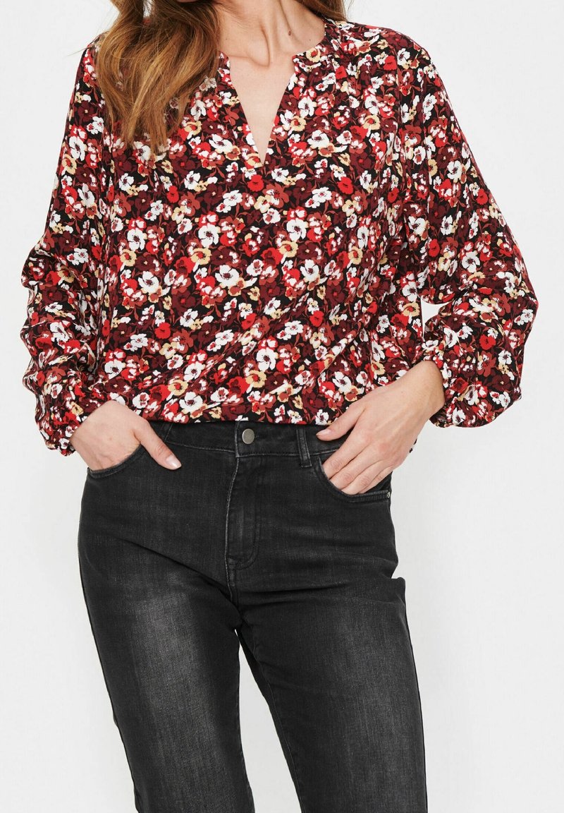 Röd blommig blus med v-ringning och knapplist, med långa puffärmar. Matchas med åtsittande svarta jeans.