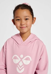 Rosa Kapuzenpulli mit einer Kängurutasche, ausgestattet mit einem großen weißen Grafikdesign auf der Vorderseite, aus weichem Stoff und in lockerer Passform mit Kapuze.