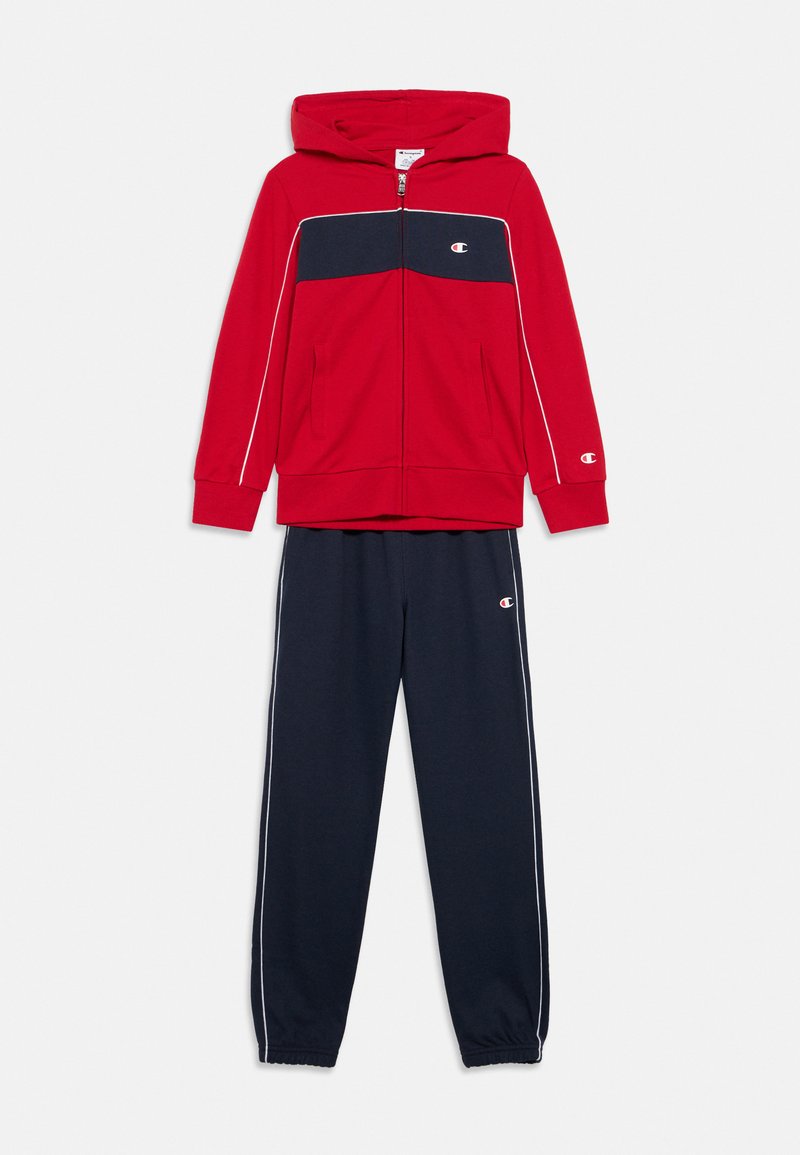 Κόκκινο φούτερ με φερμουάρ και ναυτικά στοιχεία· διαθέτει κουκούλα, μπροστινές τσέπες και λευκή ρίγα. Συνδυάζεται με ναυτικό παντελόνι jogger με ριμπ μανσέτες.