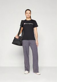 Black cotton t-shirt with white "Champion" logo, paired with gray wide-leg pants and white sneakers. A black fabric shoulder bag is held.