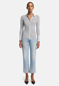 Maglione grigio a coste con bottoni e colletto a punta, abbinato a jeans cropped blu chiaro con dettagli in perline sull'orlo. Indossati scarpe ballerine nere con punta.