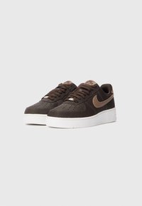 Tamno smeđi Nike Air Force 1 tenisice s teksturiranim gornjim dijelom, svijetlosmeđi swoosh i oznaka na jeziku, bijela gumena potplat, prikazane jedna do druge na sivoj pozadini.