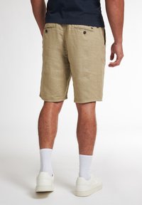 Beige Leinen-Shorts mit einer entspannten Passform, zwei Gesäßtaschen und einer glatten Textur, kombiniert mit weißen Socken und Schuhen.