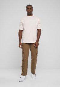 Lyserød T-shirt med korte ærmer og brune cargo-bukser med lommer, båret med hvide sneakers. Enkel design med en afslappet pasform.