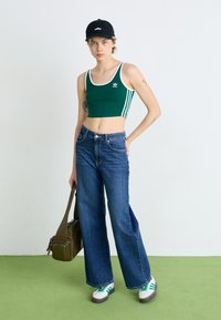 Grön crop top med vit kant och tre vita ränder, tillsammans med vida blå jeans. Tillbehör inkluderar en svart keps och skor med gröna accenter.
