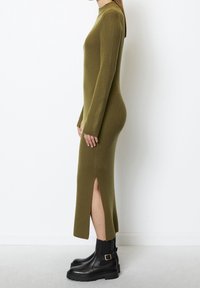 Robe longue côtelée vert olive avec des manches longues et des fentes sur les côtés, associée à des bottines noires à semelle épaisse et détail de boucle.