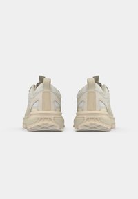 Beżowe sneakersy sportowe z teksturowaną cholewką, pętlą do zakupu i syntetycznymi akcentami. Gruba podeszwa z wzorzystym bieżnikiem dla lepszej przyczepności. Widok z tyłu.