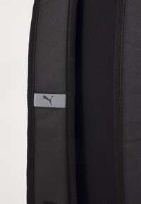 Čierny batoh s textúrovaným povrchom, so sivým obdĺžnikovým akcentom a logom Puma. Dizajn je zjednodušený s vystuženými okrajmi.