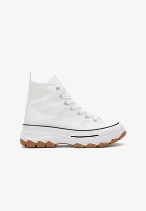 Zapatilla blanca de caña alta con cordones blancos, suela blanca gruesa y suela exterior marrón texturizada para un agarre extra, vista lateral sobre fondo blanco.
