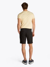 Calções pretos com bainhas dobradas, usados com uma t-shirt amarela clara, complementados por ténis azul-marinho. A vista traseira destaca o design casual.