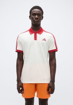 Polohemd in Off-White mit rotem Kragen und Ärmeln, versehen mit roten Akzentstreifen und einem kleinen Logo auf der linken Brustseite.