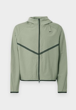 Light green athletic jacket with a zippered front, hood, and contrasting dark green accents. Features long sleeves and a fitted design.