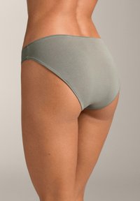 Zelené bavlnené bikini spodné prádlo s bezšvovým dizajnom, jemnou textúrou a stredne vysokým pásom, ktoré predvádza hladký obrys zadočku.