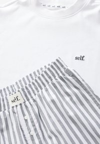 Vit bomull t-shirt med broderi av "self." och grårandiga pyjamasbyxor med elastisk midja och knapprad, med en tygetikett.