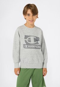 Felpa grigia con logo "Champion" testurizzato, scollatura rotonda e polsini a coste, abbinata a pantaloni della tuta verdi. Tessuto morbido e casual.