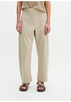 Beige High-Waist Hose mit weitem Bein und aufgesetzten Fronttaschen, getragen mit braunen flachen Sandalen mit Riemchen und einem locker gestrickten beigen Top.