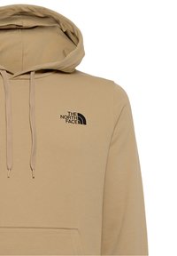 Sudadera beige con cordones, bolsillo frontal y un logo negro en el lado izquierdo del pecho. Hecha de un material suave y elástico.
