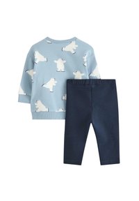 Jasnoniebieska bluza z białym nadrukiem polarnym niedźwiedzia, w połączeniu z granatowymi legginsami. Bluza ma prążkowane mankiety i okrągły dekolt.