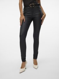 Sorte smale bukser i kunstlær med høy midje og belte med gullfarget ovalt spenne, kombinert med offwhite spisse hæler.