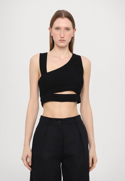 Sort ribbet crop top med asymmetrisk design, brede stropper og udskæringsdetaljer. Stylet med højtaljede sorte bukser.
