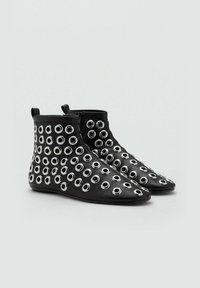 Botas negras hasta el tobillo con un acabado de cuero suave, con ojales de metal en diferentes tamaños en la superficie. Punta afilada y cierre de cremallera.