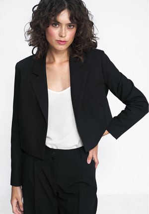 Czarna krótka marynarka o dopasowanym kroju, z klapami i długimi rękawami; noszona na białej bluzce. Gładki materiał, minimalistyczny design.
