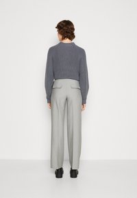 Szara, dziergana crop sweater o ryflowanej strukturze w połączeniu z wysokimi, dopasowanymi szarymi spodniami. Widać czarne buty na grubej podeszwie.