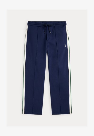 Pantalon jogger bleu marine avec des bandes latérales blanches et vertes, taille à cordon, poches avant, et petit logo blanc brodé sur la cuisse droite.