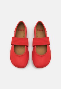 Zapatos Mary Jane de cuero rojo con una amplia correa elástica. Diseño de punta redondeada y textura suave. Interior forrado con el logotipo de la marca visible.