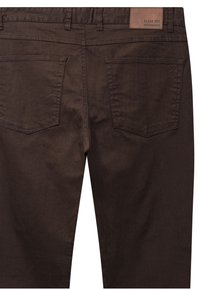 Ruskeat denimpöksyt, joissa on kaksi takataskua, vyölenkit ja nahkainen merkintä "Clean Cut Copenhagen" vyötäröllä.