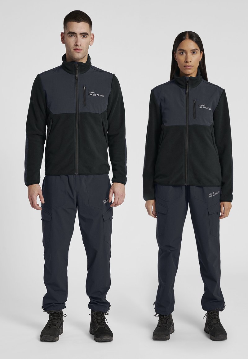 Zwarte en donkergrijze fleece jassen met een ritssluiting aan de voorkant, gecombineerd met marineblauwe cargo broeken met zakken. Beide dragen zwarte laarzen.