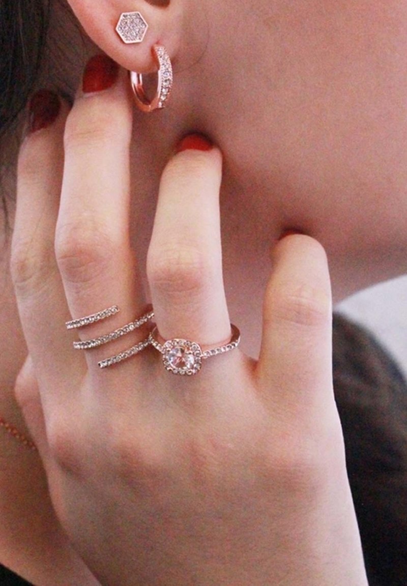 I gioielli in oro rosa presentano: un orecchino a forma esagonale, un cerchio scintillante e anelli multipli con design intricati e una gemma centrale.