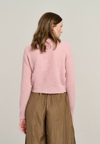 Rosa gestrickter Pullover mit einem verkürzten Design, strukturiertem Finish und geripptem Saum. Kombination mit einem braunen, glänzenden, plissierten Rock.