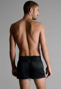 Un maillot de bain noir en tissu lisse, avec une taille élastique et un design simple. Vu de dos, sans détails supplémentaires.