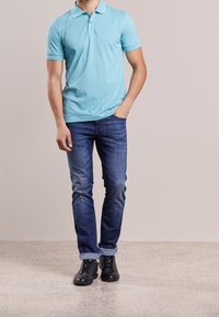Polo shirt bleu clair à manches courtes, avec un col et un bouton unique, associé à un jean en denim foncé et des baskets noires.